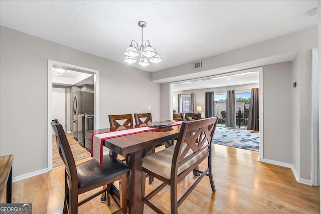 dining room featuring light hardwood / wood-style floors, washer and clothes dryer, and a notable chandelier