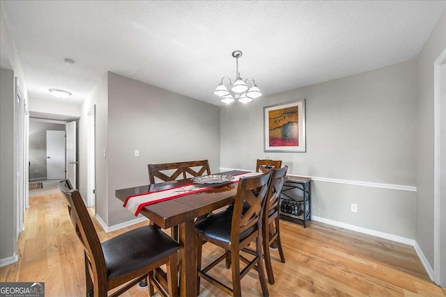 dining area featuring light wood-type flooring, a textured ceiling, and a notable chandelier