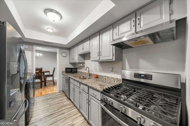 kitchen featuring light stone countertops, decorative backsplash, stainless steel appliances, sink, and light hardwood / wood-style floors