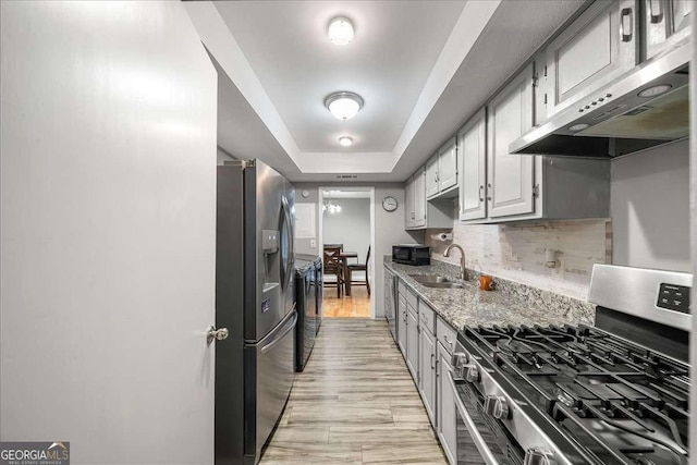 kitchen featuring light stone countertops, decorative backsplash, stainless steel appliances, a raised ceiling, and sink