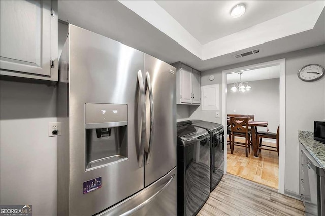 kitchen featuring independent washer and dryer, a notable chandelier, pendant lighting, appliances with stainless steel finishes, and light wood-type flooring