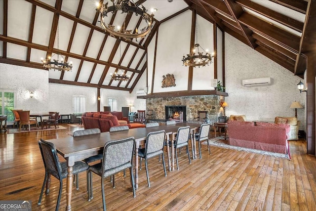 dining area featuring high vaulted ceiling, a stone fireplace, hardwood / wood-style flooring, a wall unit AC, and a chandelier