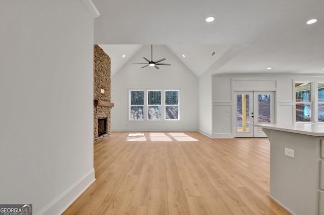 unfurnished living room with light hardwood / wood-style floors, a stone fireplace, ceiling fan, plenty of natural light, and lofted ceiling