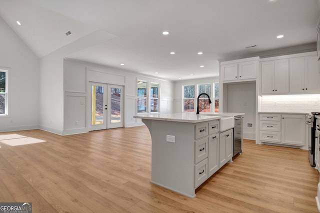 kitchen with sink, white cabinetry, french doors, and an island with sink