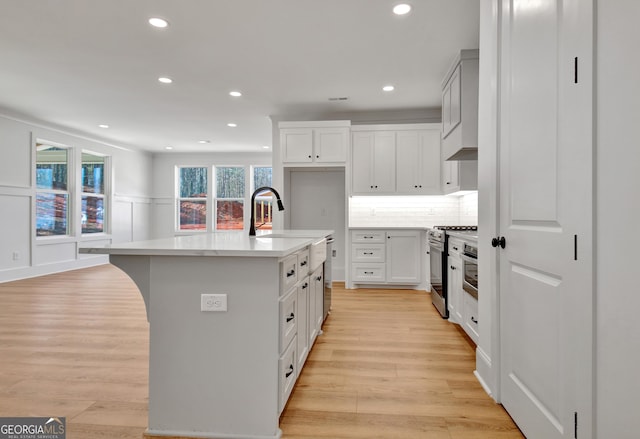 kitchen featuring a center island with sink, sink, white cabinetry, and stainless steel stove