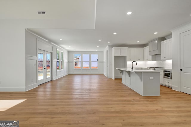 kitchen featuring a center island with sink, a kitchen bar, white cabinetry, light hardwood / wood-style flooring, and french doors