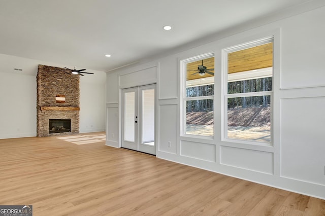 unfurnished living room with light wood-type flooring, french doors, and a stone fireplace