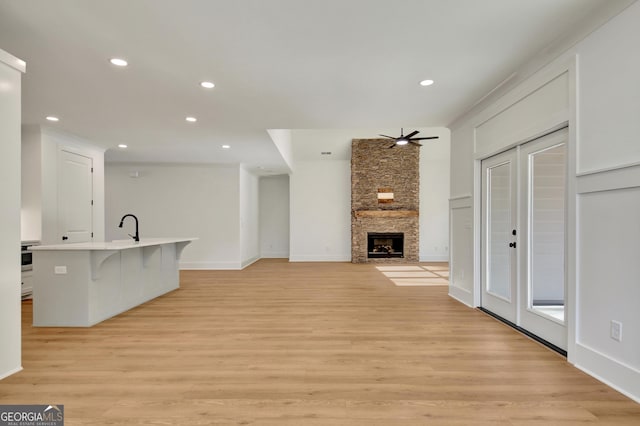 unfurnished living room featuring ceiling fan, sink, light wood-type flooring, and a fireplace