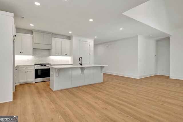 kitchen with white cabinetry, a center island with sink, stainless steel gas range oven, a breakfast bar area, and light wood-type flooring