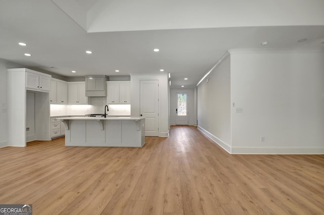 kitchen with white cabinetry, tasteful backsplash, a kitchen island with sink, crown molding, and light hardwood / wood-style flooring