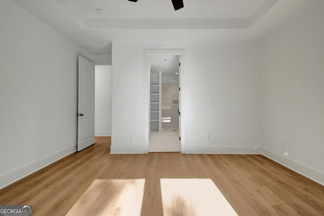 spare room featuring ceiling fan, light wood-type flooring, and a tray ceiling