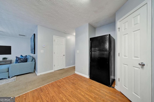 kitchen with black refrigerator, a textured ceiling, and light hardwood / wood-style floors