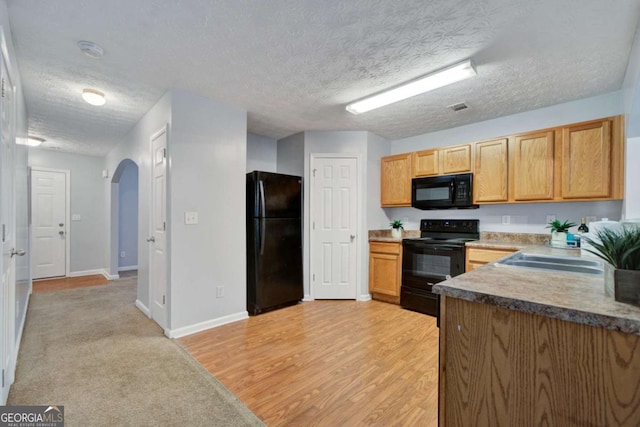 kitchen featuring sink, black appliances, a textured ceiling, and light hardwood / wood-style floors