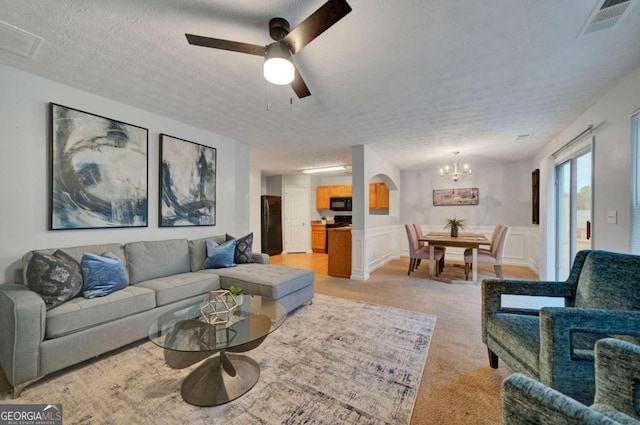 living room with ceiling fan with notable chandelier, light colored carpet, and a textured ceiling