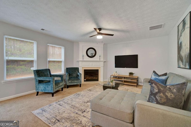 living room with ceiling fan, a fireplace, light colored carpet, and a textured ceiling