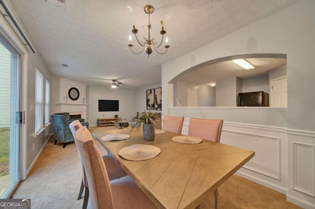 carpeted dining room with ceiling fan with notable chandelier and a textured ceiling