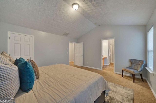 bedroom featuring light colored carpet, lofted ceiling, a textured ceiling, and ensuite bath