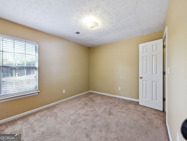 spare room featuring a textured ceiling and light colored carpet