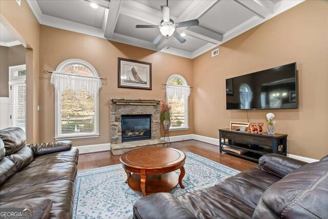 living room with beam ceiling, ceiling fan, coffered ceiling, a stone fireplace, and hardwood / wood-style flooring