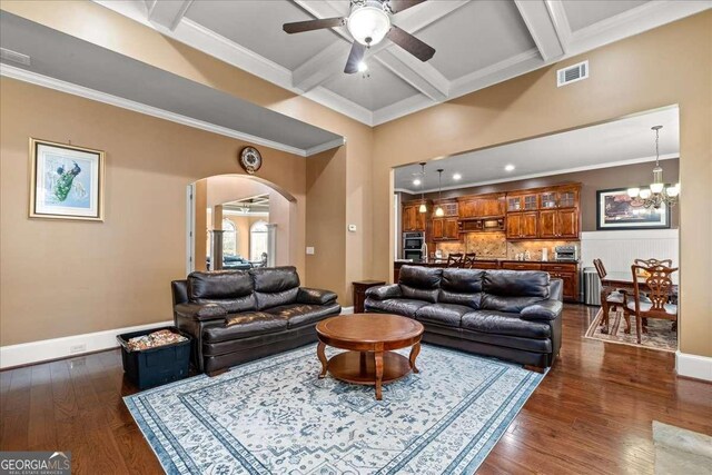 living room with coffered ceiling, beamed ceiling, ceiling fan with notable chandelier, and ornamental molding