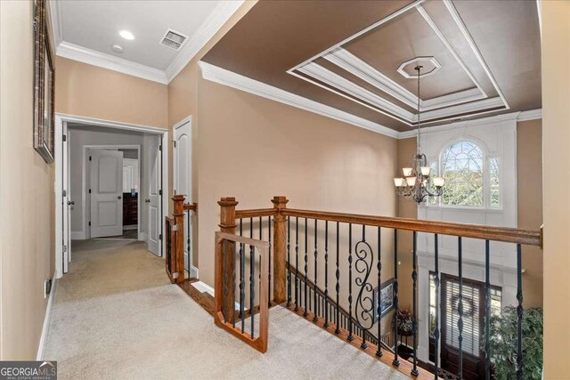 hall featuring a chandelier, light carpet, a tray ceiling, and ornamental molding