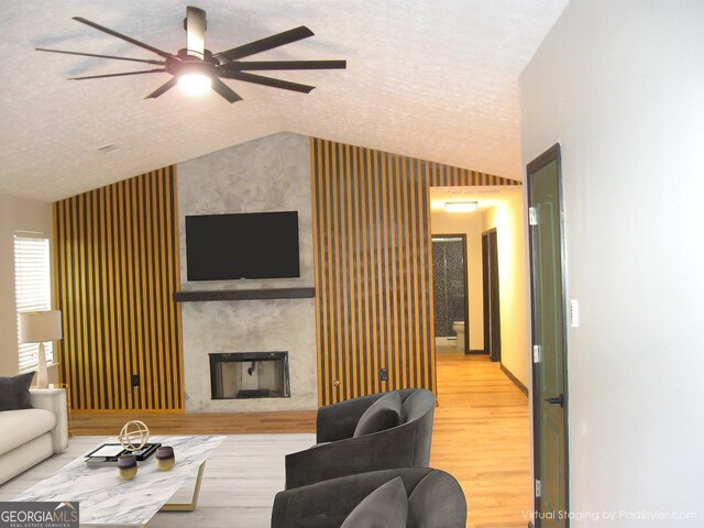 living room with a textured ceiling, light wood-type flooring, ceiling fan, and lofted ceiling