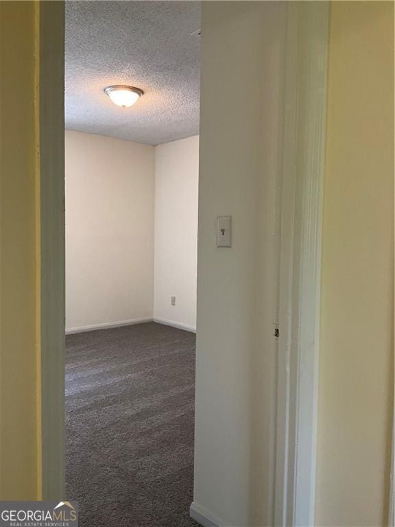 corridor featuring dark carpet and a textured ceiling