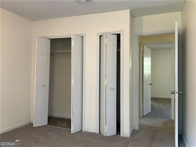 unfurnished bedroom with multiple closets, carpet floors, and a textured ceiling