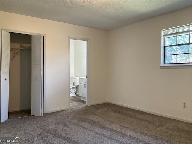 unfurnished bedroom featuring dark colored carpet, a textured ceiling, ensuite bath, and a closet