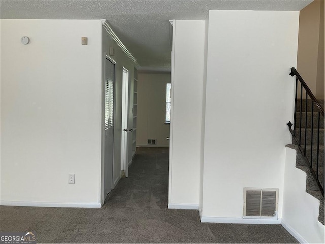 hall with crown molding, dark carpet, and a textured ceiling