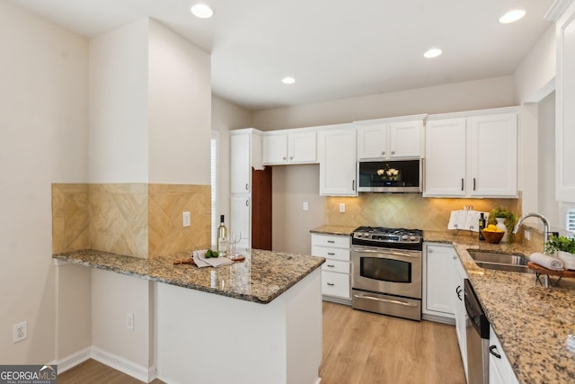 kitchen with appliances with stainless steel finishes, stone counters, kitchen peninsula, white cabinets, and light hardwood / wood-style flooring