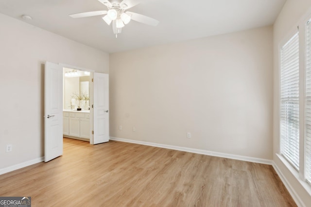 unfurnished bedroom with ceiling fan, ensuite bath, light wood-type flooring, and multiple windows