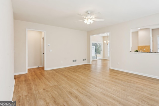 empty room featuring ceiling fan with notable chandelier and light hardwood / wood-style flooring