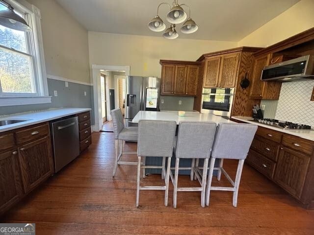 kitchen featuring a kitchen bar, appliances with stainless steel finishes, backsplash, dark hardwood / wood-style floors, and range hood