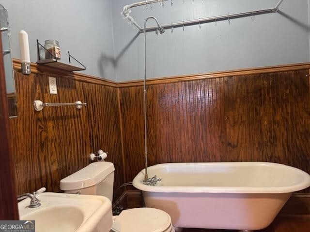 bathroom featuring a tub to relax in, toilet, wooden walls, and sink