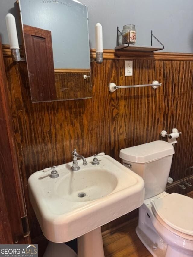 bathroom with wood walls, sink, wood-type flooring, and toilet