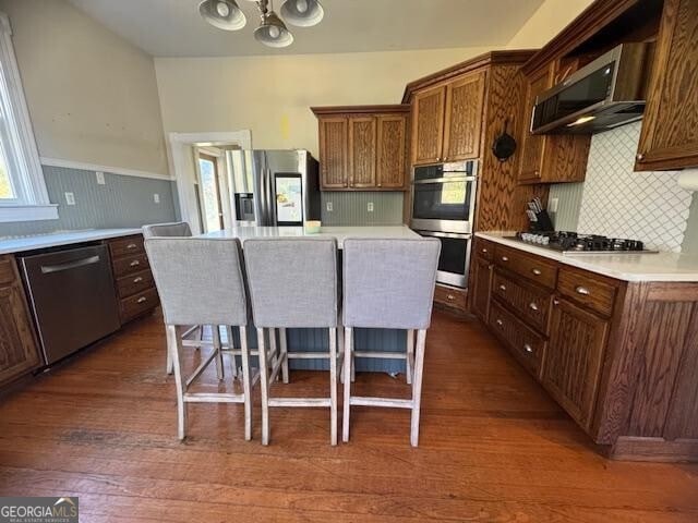 kitchen with backsplash, a breakfast bar, stainless steel appliances, dark wood-type flooring, and a kitchen island