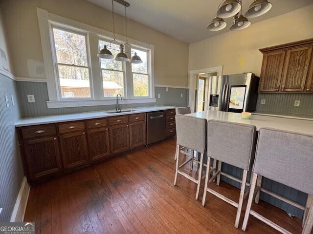 kitchen with a kitchen breakfast bar, stainless steel appliances, dark wood-type flooring, sink, and hanging light fixtures