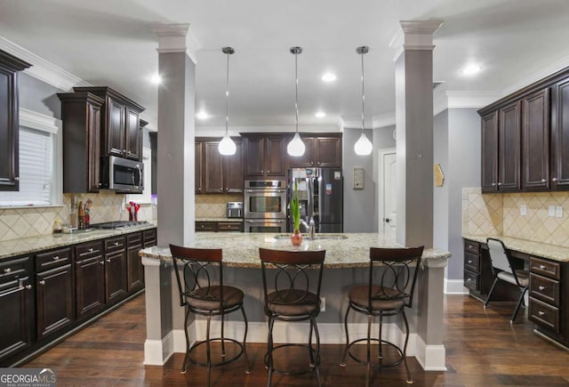 kitchen with appliances with stainless steel finishes, hanging light fixtures, and a kitchen island with sink