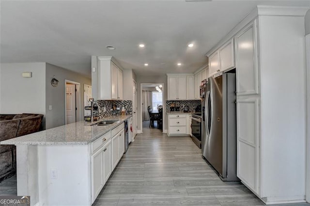 kitchen with kitchen peninsula, light stone counters, stainless steel appliances, sink, and white cabinets