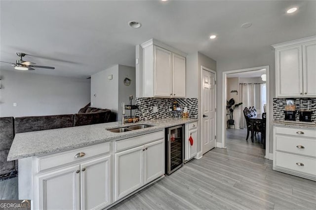 kitchen with white cabinetry, sink, beverage cooler, light stone counters, and kitchen peninsula