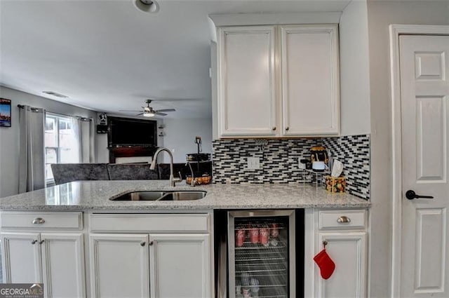 kitchen featuring light stone countertops, sink, white cabinets, and beverage cooler