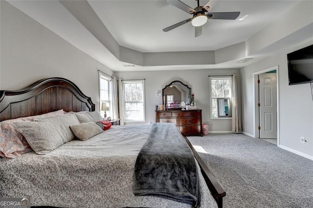 carpeted bedroom with multiple windows, a raised ceiling, and ceiling fan