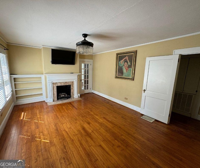 unfurnished living room with hardwood / wood-style floors, a textured ceiling, crown molding, and a brick fireplace