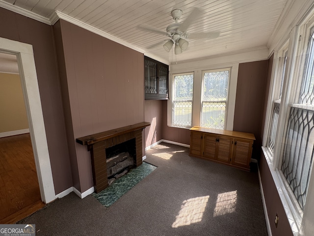 unfurnished living room with ceiling fan, crown molding, dark carpet, and a brick fireplace