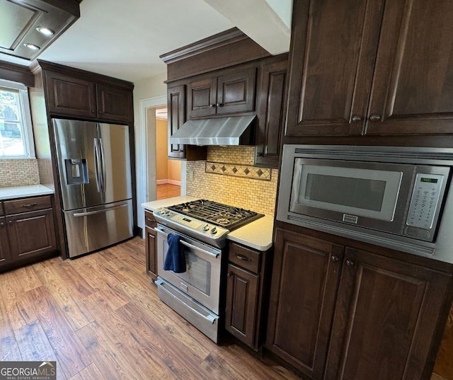 kitchen with stainless steel appliances, tasteful backsplash, light hardwood / wood-style flooring, ventilation hood, and dark brown cabinets