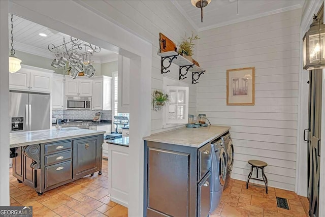 kitchen featuring washing machine and clothes dryer, white cabinetry, crown molding, a breakfast bar, and appliances with stainless steel finishes