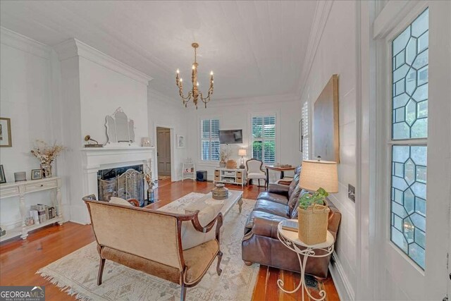 living area with ornamental molding, a fireplace, an inviting chandelier, and wood finished floors