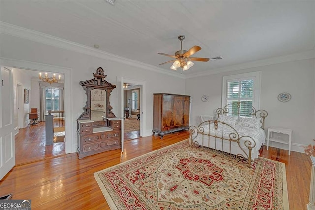 bedroom featuring ceiling fan with notable chandelier, light hardwood / wood-style floors, and crown molding