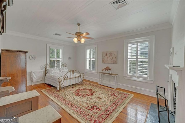 bedroom featuring crown molding, a fireplace with flush hearth, wood finished floors, and visible vents